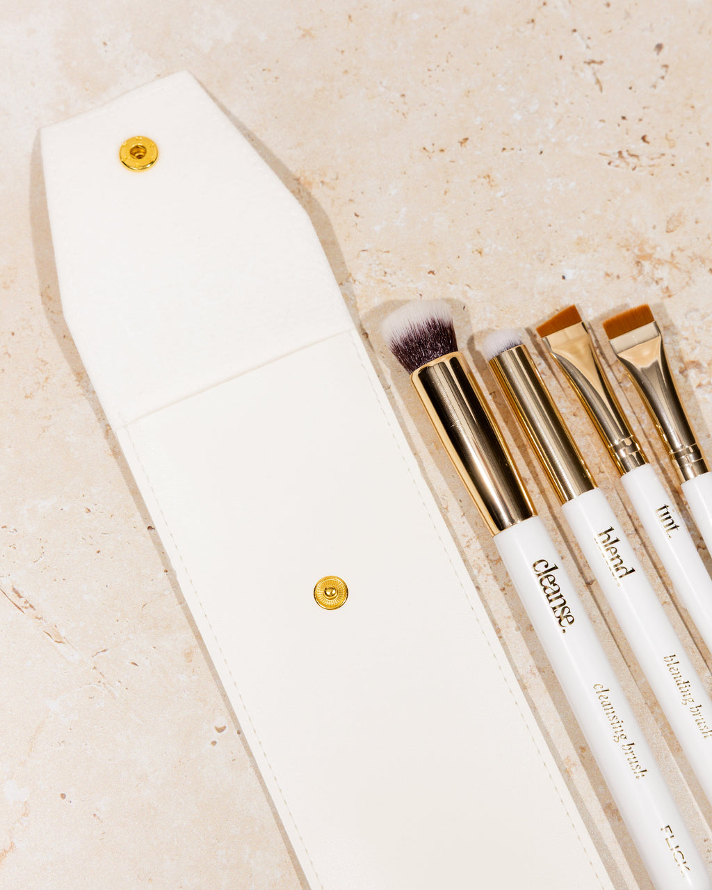 Set of makeup brushes with white handles and gold accents on a beige background